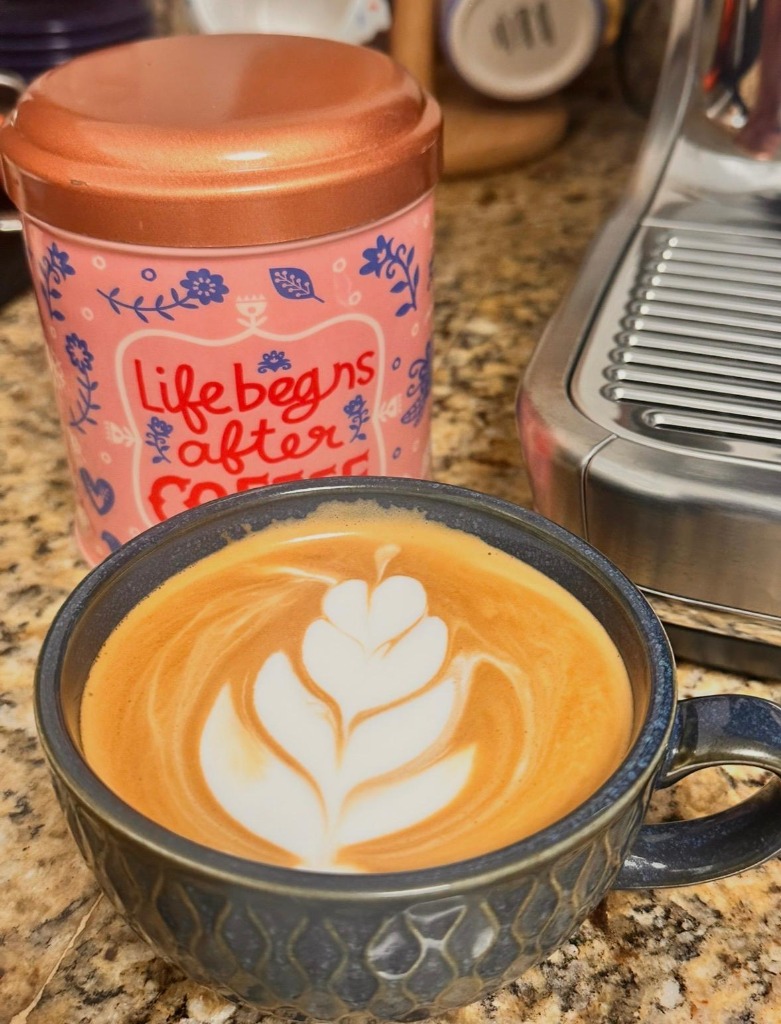 A beautiful latte art pour next to a coffee tin